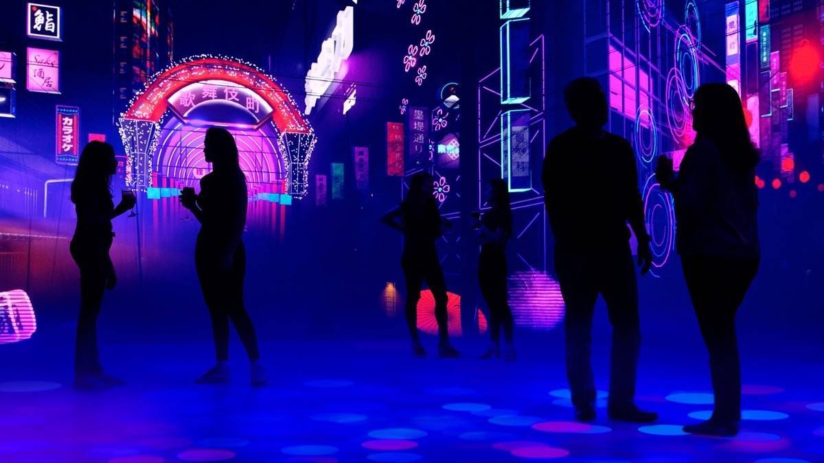 Several people standing in a bar that is lit with blue and pink asian inspired lighting