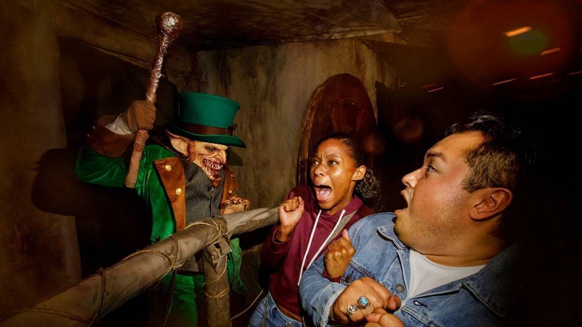 An scary leprechaun waving a large club while scaring two people