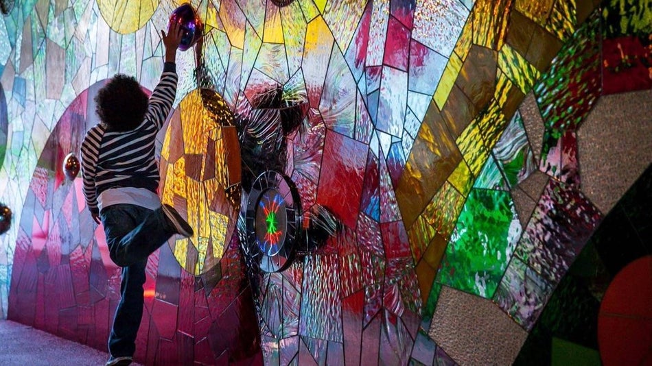 Little boy jumping up on one leg to touch a large gem on a brightly colored wall