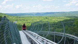 Wide view of a alpine coaster as a rider starts to descend a hill with the green ozark mountains in the background