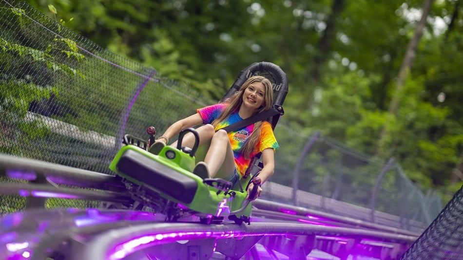 A girl in a tie dye shirt on a coaster chair riding through an alpine coaster