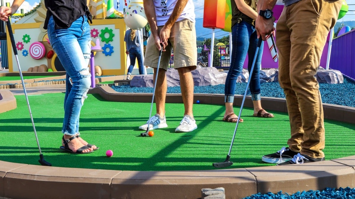 Several friends holding putting clubs on a green at a mini golf course