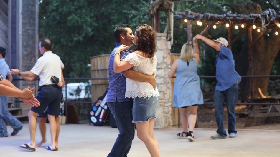 Couples dancing on a concrete dance floor with woods and hanging lights in the background