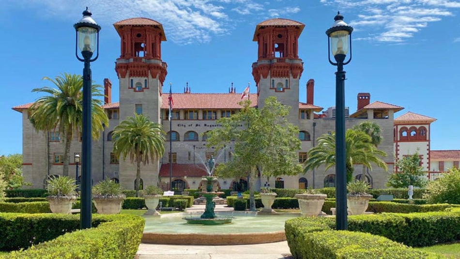 Exterior shot of old spanish style stone building with palm trees and shrubbery