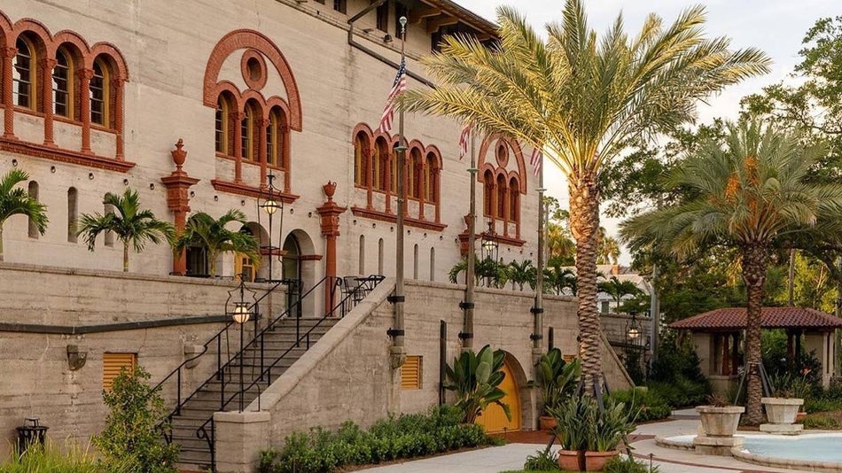 Exterior shot of old spanish style stone building with palm trees and shrubbery