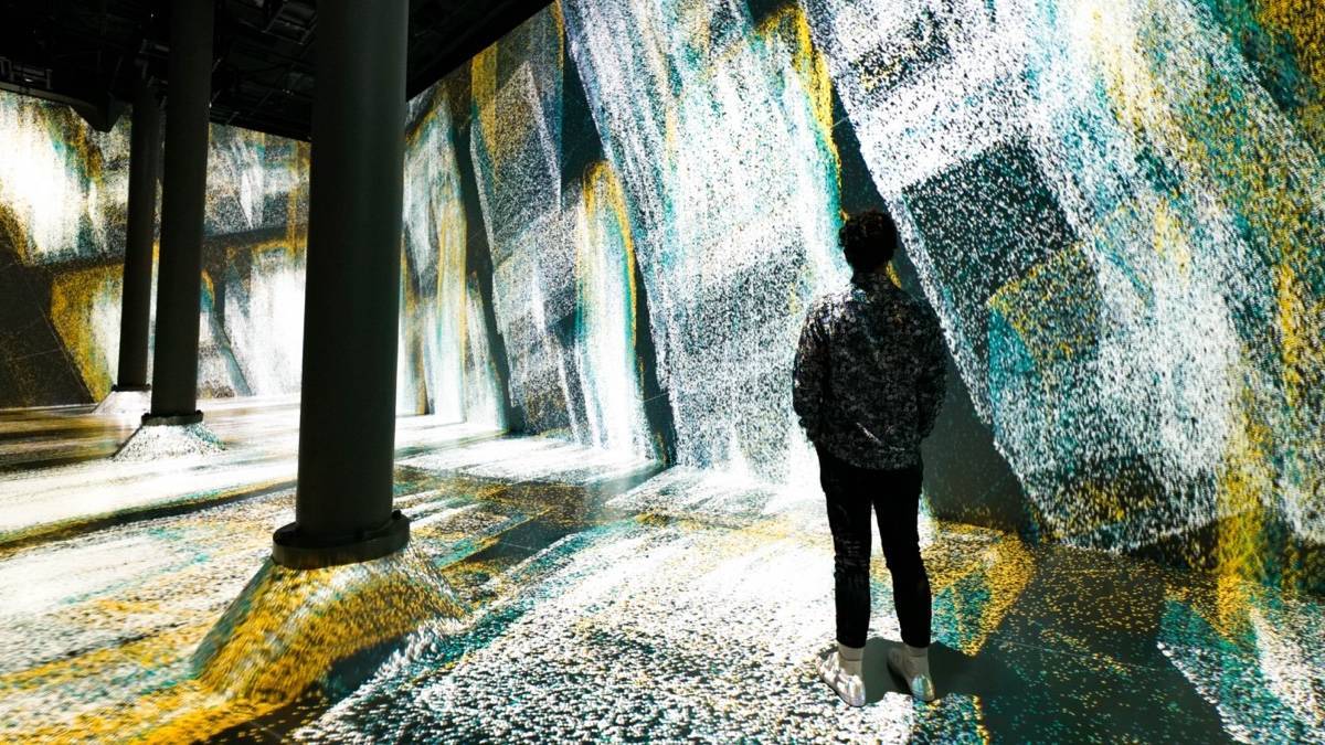 A person standing in a room looking at an art installation that takes up an entire wall and the floor