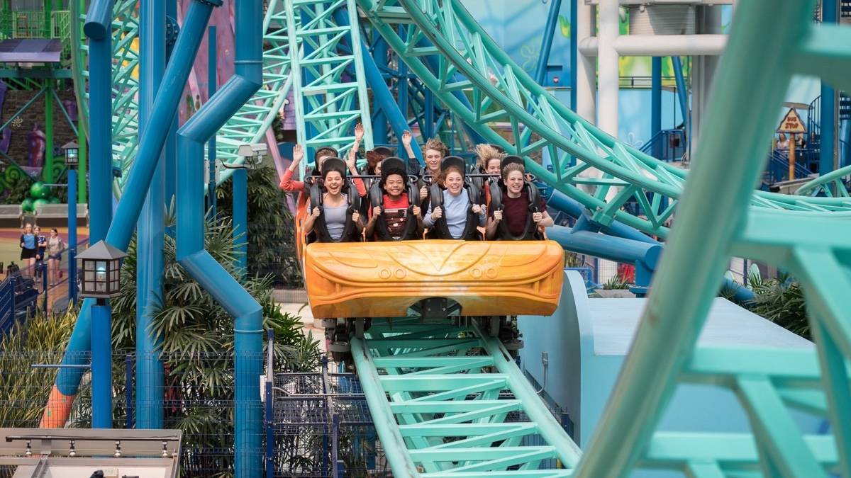 People riding in an orange roller coaster car on a bright blue track