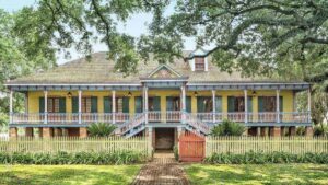 Front exterior of yellow and blue painted plantation house with a brick sidewalk and a huge oak tree
