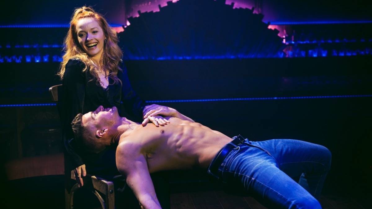 Close up of a woman sitting in a chair with a fit shirtless man laying backwards on her