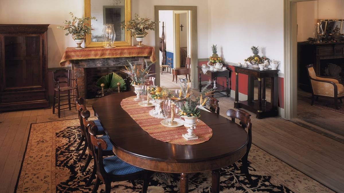 Interior dining room of a plantation house with a dining table, chairs, fireplace and other furniture surrounding
