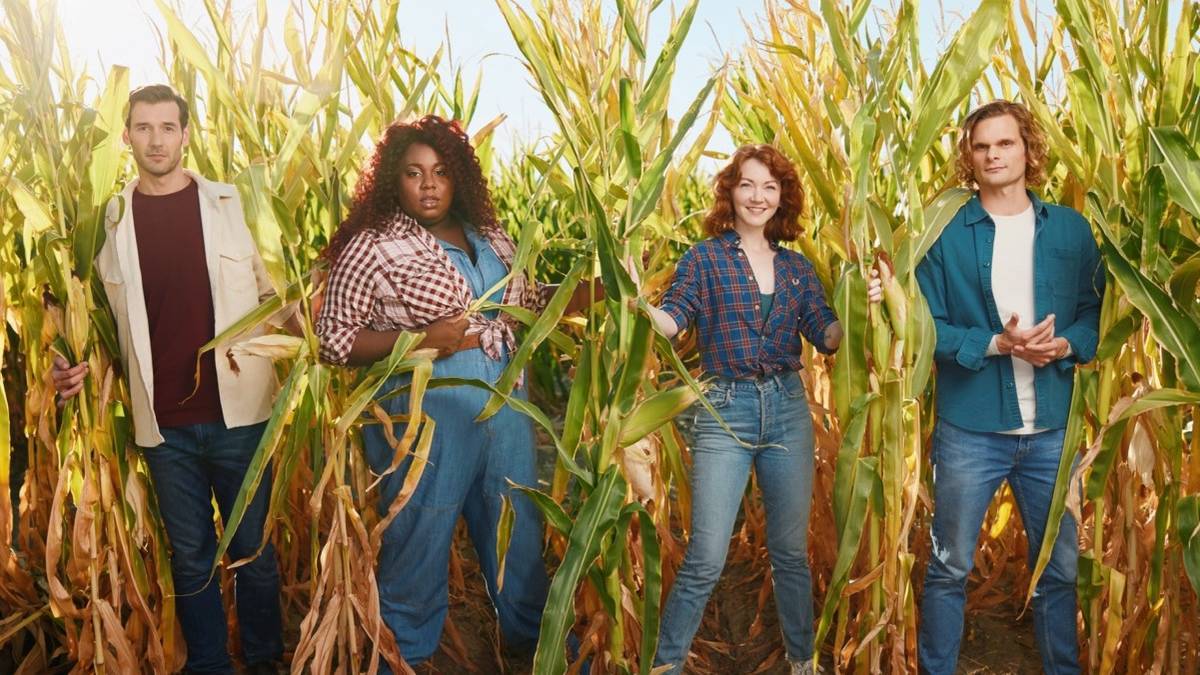 Four people in farm attire standing among corn stalks