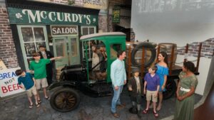 Family next to an old green truck that's holding barrels in front of a saloon