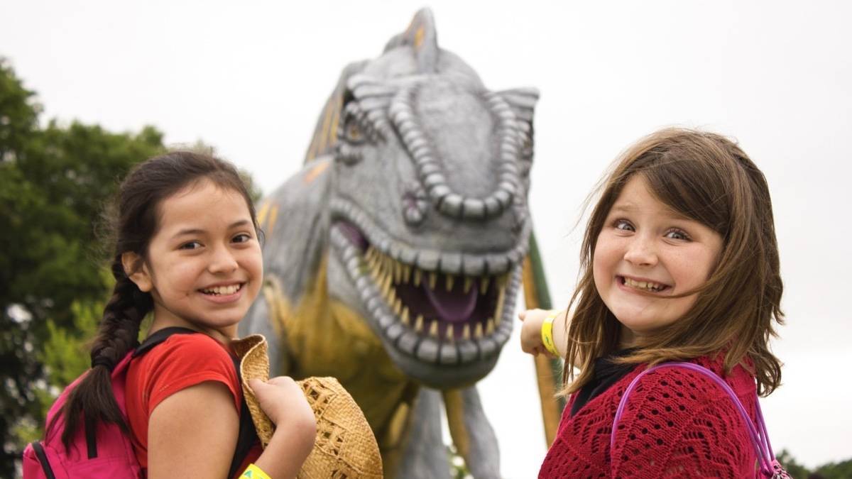 Two kids smiling with a model TRex in the background