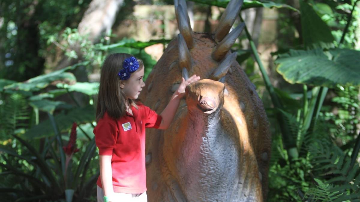 Small girl petting a dinosaur with tropical plants surrounding them