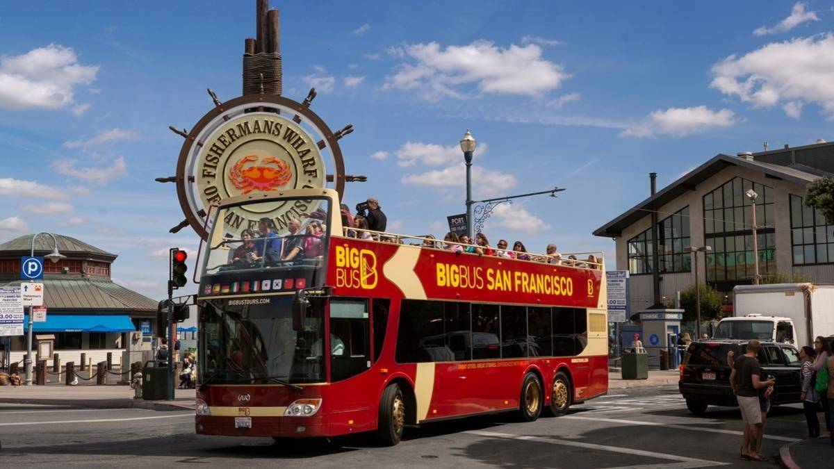 Red bus next to the Fisherman's Wharf sign under a blue sky