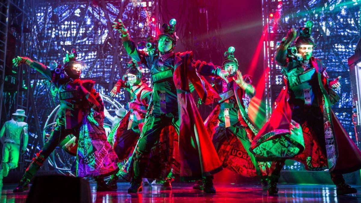 Several performers on a stage in elaborate costumes surrounded by red and green light