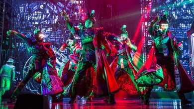 Several performers on a stage in elaborate costumes surrounded by red and green light