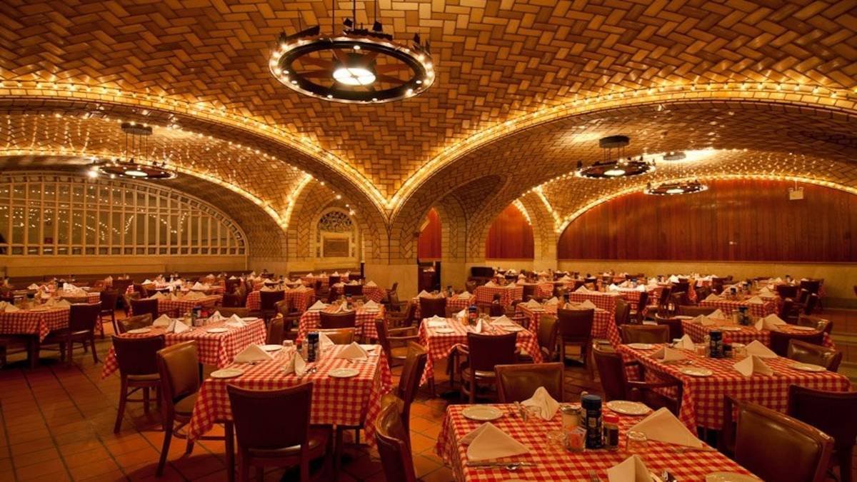 Wide shot of a dining room with arched brick ceilings and red check table cloth covered tables with napkins and place settings