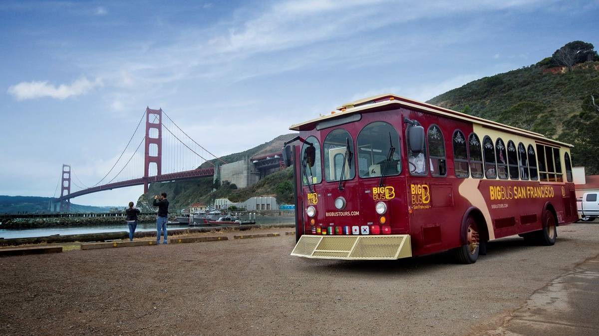 Red Big Bus parked with the golden gate bridge in the background with people taking pictures of it