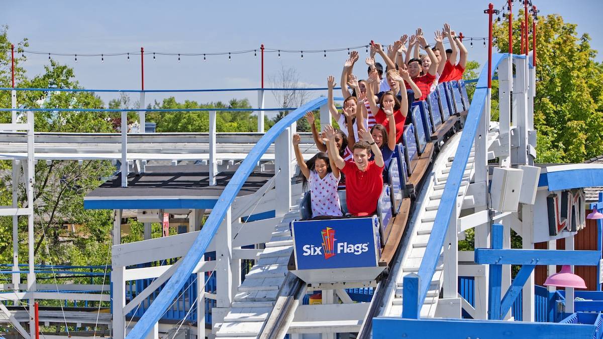 Several people on a blue and white roller coaster with their hands up