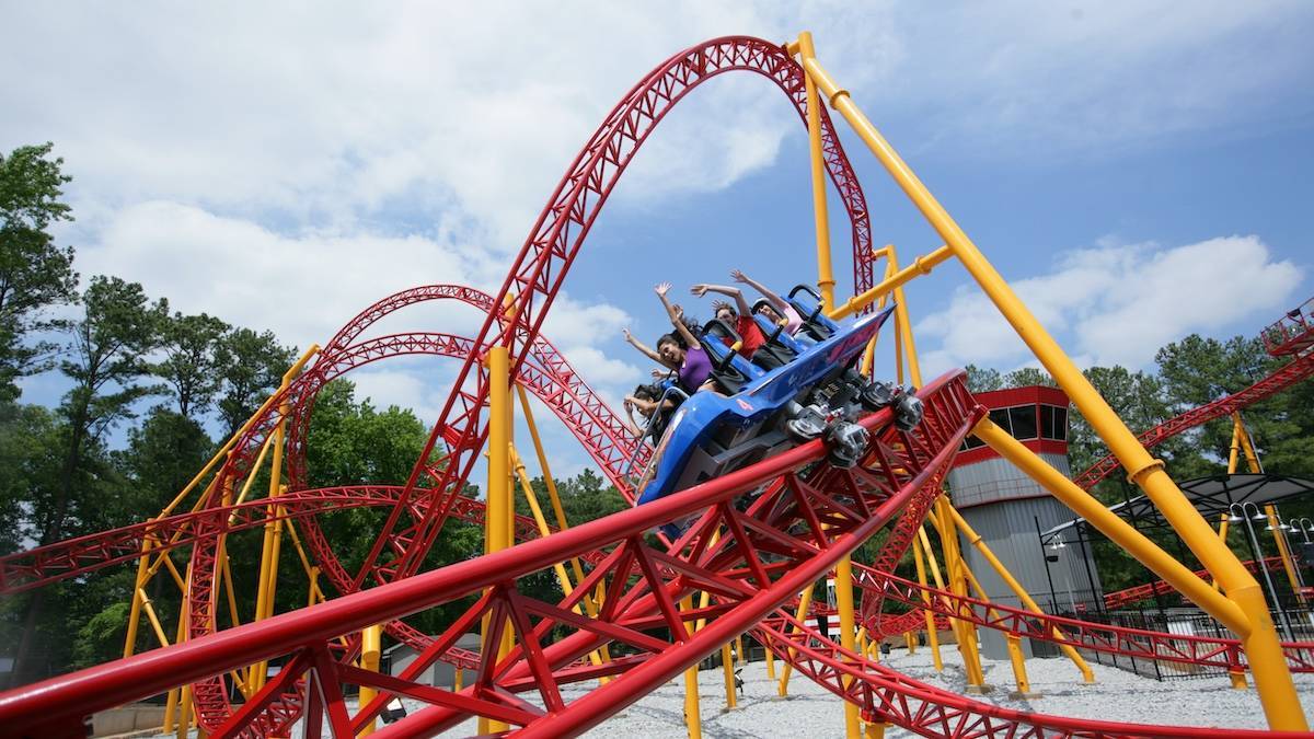 Red and yellow roller coaster with people riding with their hands up