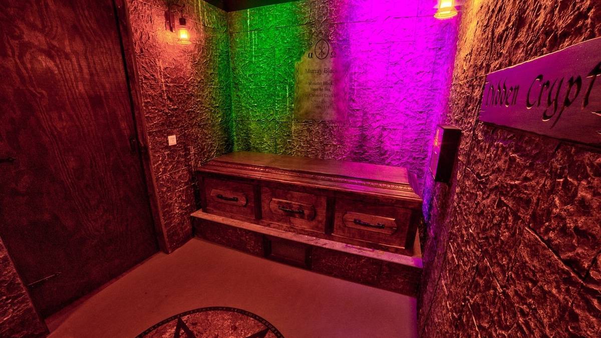 A purple and green lit room with an old chest and old rock looking walls