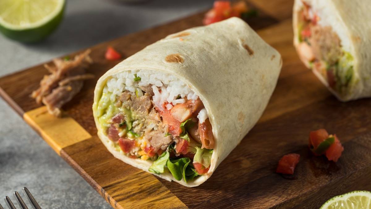 burrito with rice, meat and vegetables inside on wooden cutting board