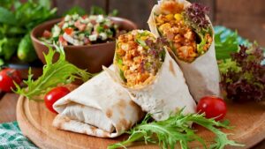 several burritos filled with meat and vegetables on wooden plate with a bowl of salsa in the background