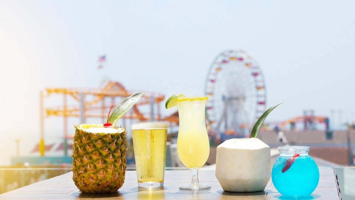 Five tropical drinks on a table with the Santa Monica Pier in the background under a blue sky