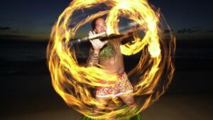 Flame performer spinning a stick with hawaiian clothing on