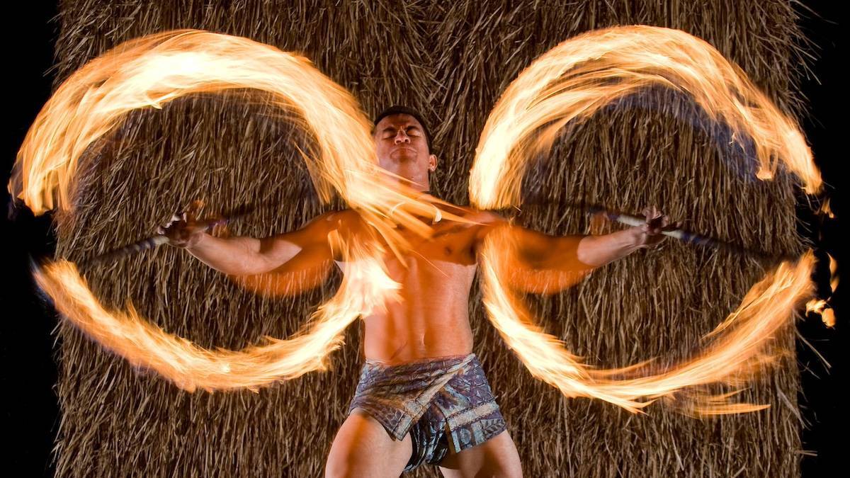Flame performer spinning two sticks with hawaiian clothing on