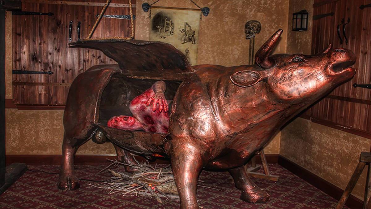 Metal bull standing over a fire with its side open and a man inside at the medieval torture museum in chicago