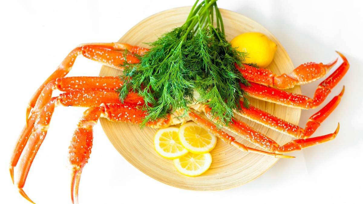 Large sets of crab legs on a wooden plate with green garnish and lemon slices around it