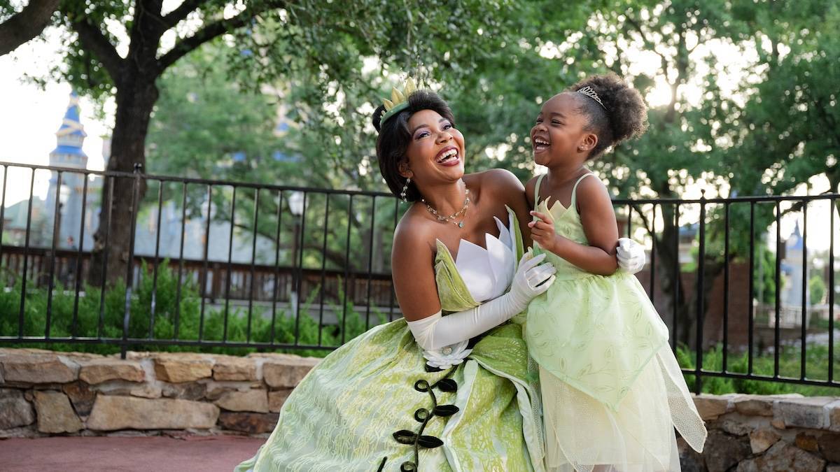 A woman and a small girl laughing and smiling while wearing green Tiana character dresses at Disney world