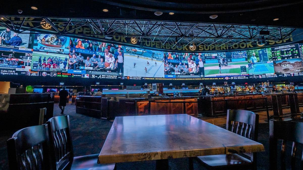 Interior of a sports bar with a full wall of tv screens and a bar with tables and chairs too