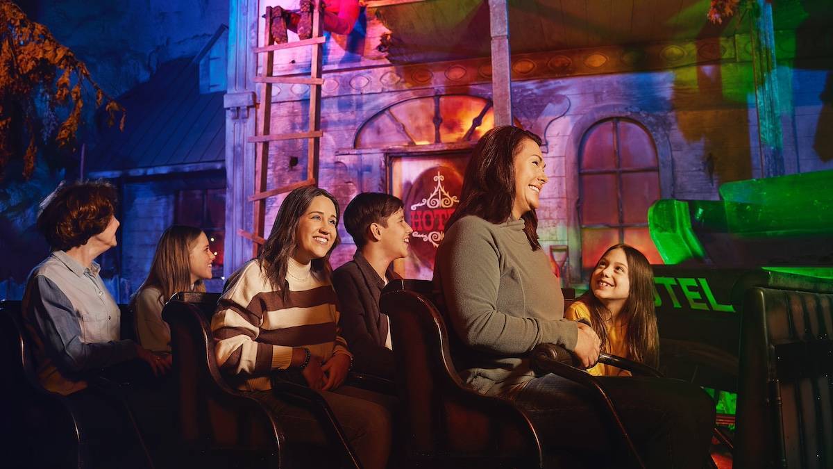Families on an indoor roller coaster car with an old wild west building in the background