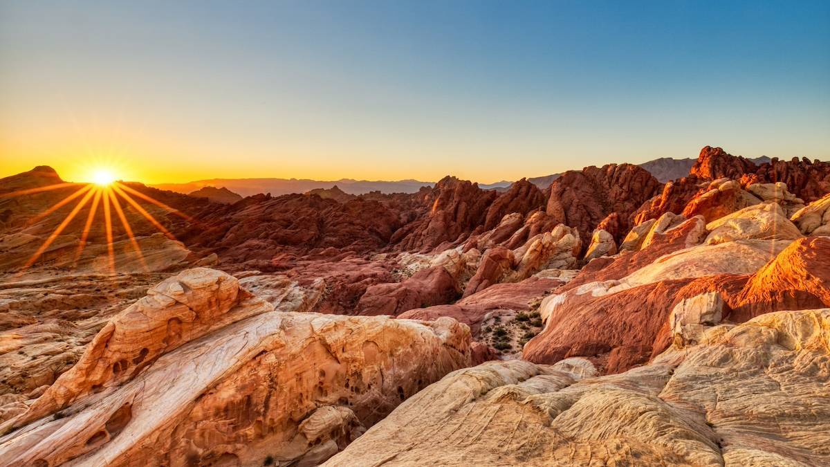 Red rock desert with the sun on the horizon under a blue sky