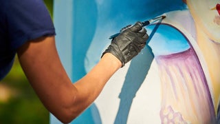 A person with black gloves on holding a paint brush to a large canvas they've been painting