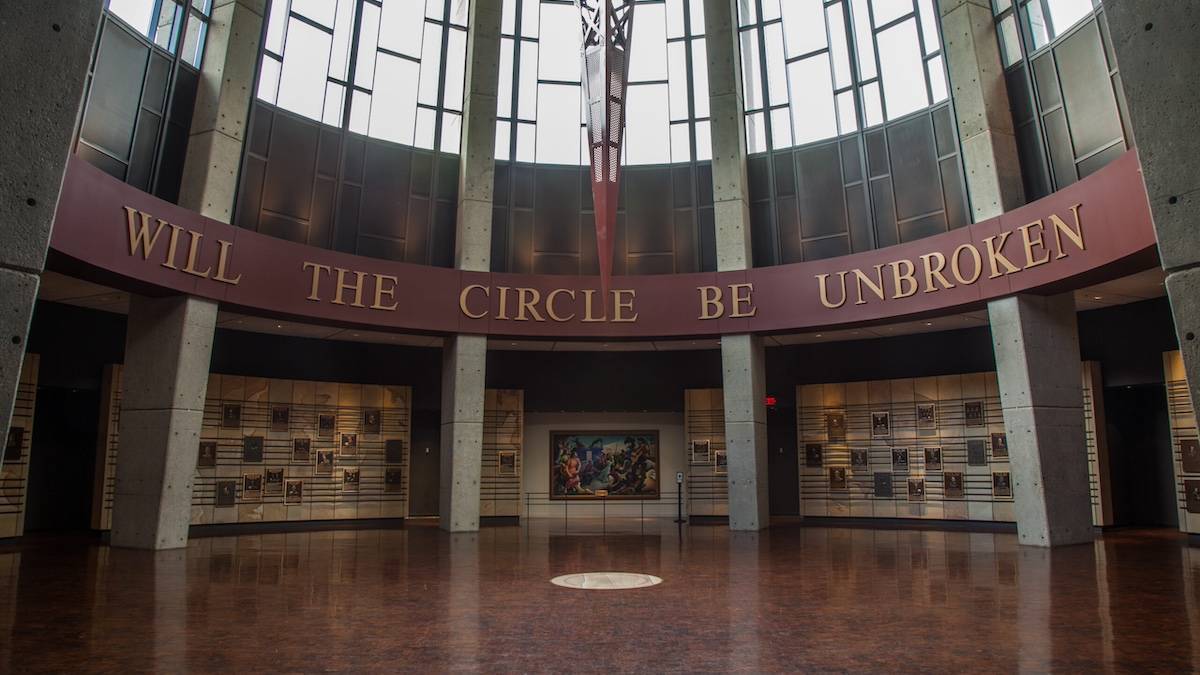 Interior rotunda with a red sign saying "will the circle be unbroken" over a wall with photos hanging
