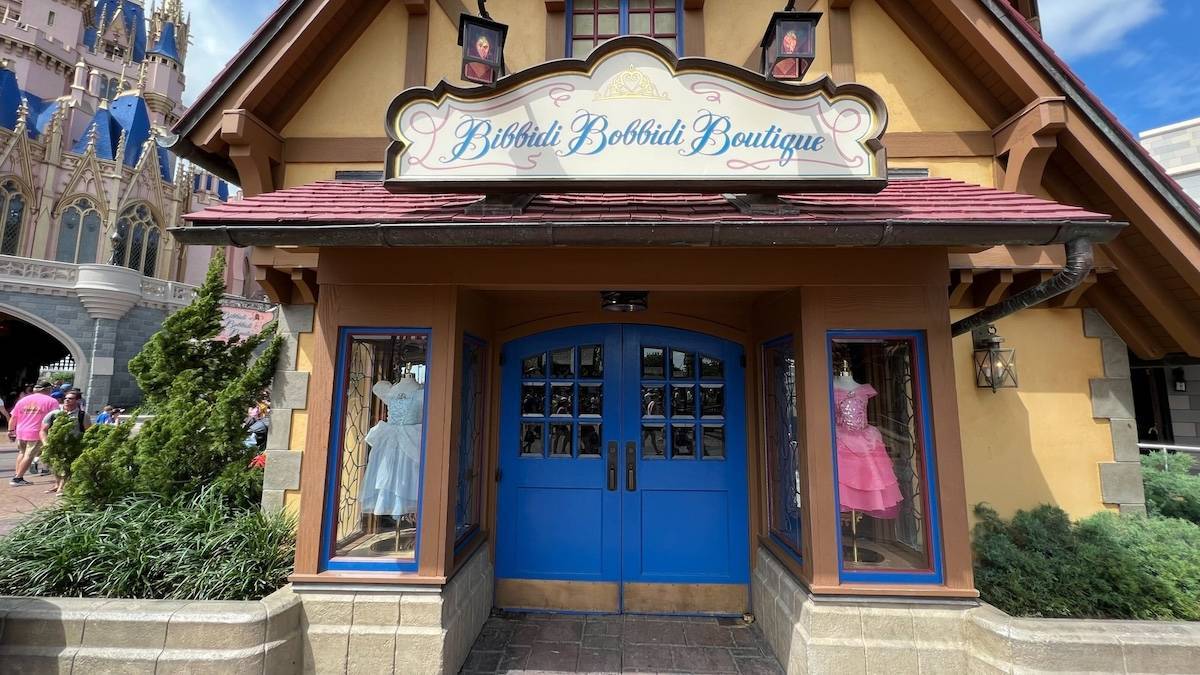 Exterior shot of Bibbidi Bobbidi Boutique shop with a blue door and Cinderella's castle in the background