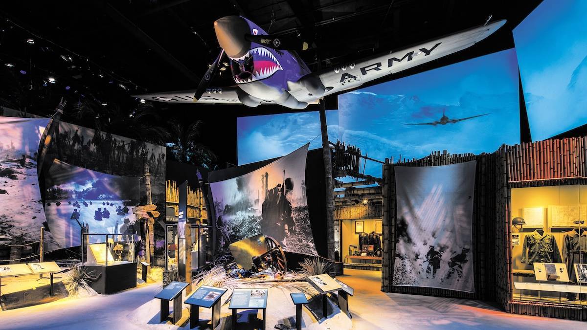 Interior shot of a room with WW2 exhibits and a US Army plane hanging from the ceiling
