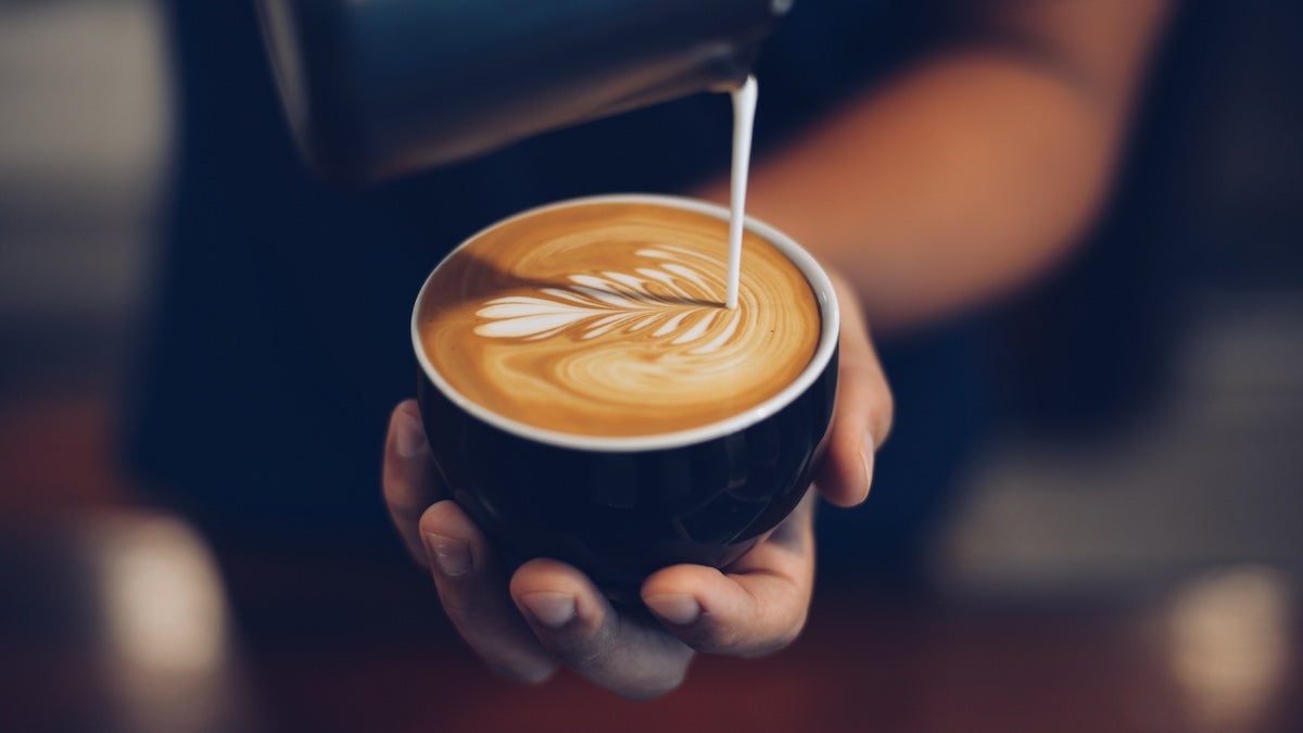 Hand holding a cup of coffee while pouring milk into it
