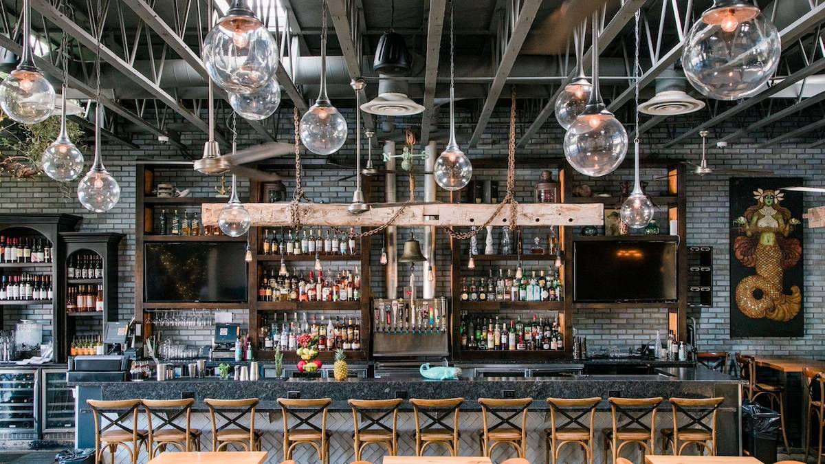 Wide shot of a bar with stools and hanging overhead lights in an industrial setting