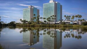 Two hotel buildings next to a lake with palm trees under blue skies