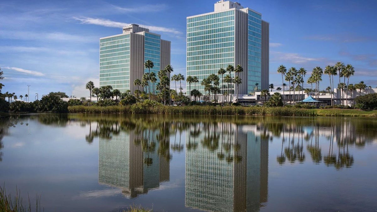 Two hotel buildings next to a lake with palm trees under blue skies