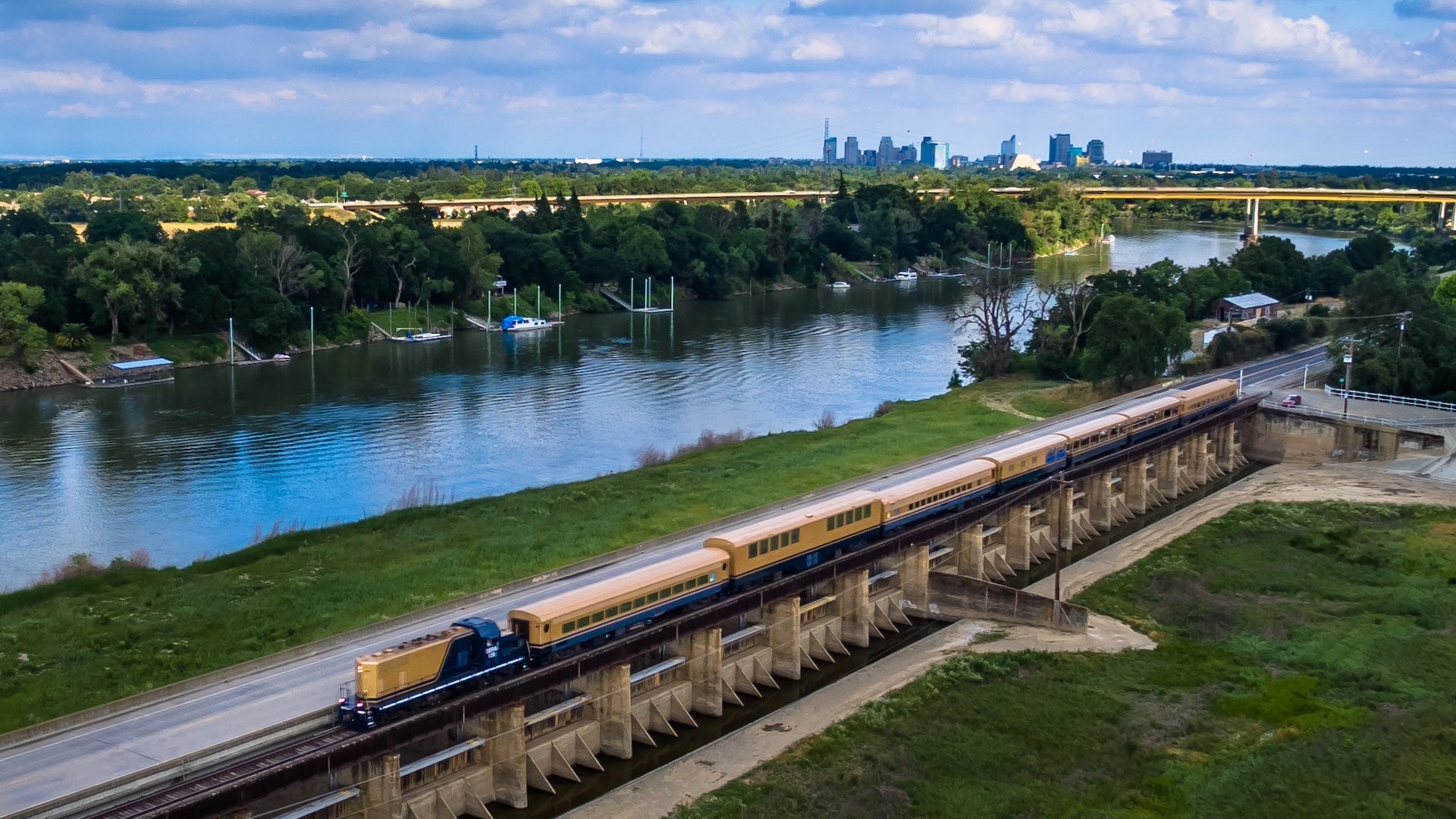 Aerial shot of a train moving next to a river with a city in the background