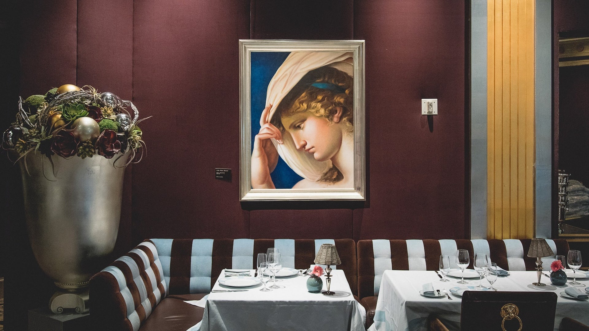 Fine art on a maroon wall with tables and striped booths beneath it