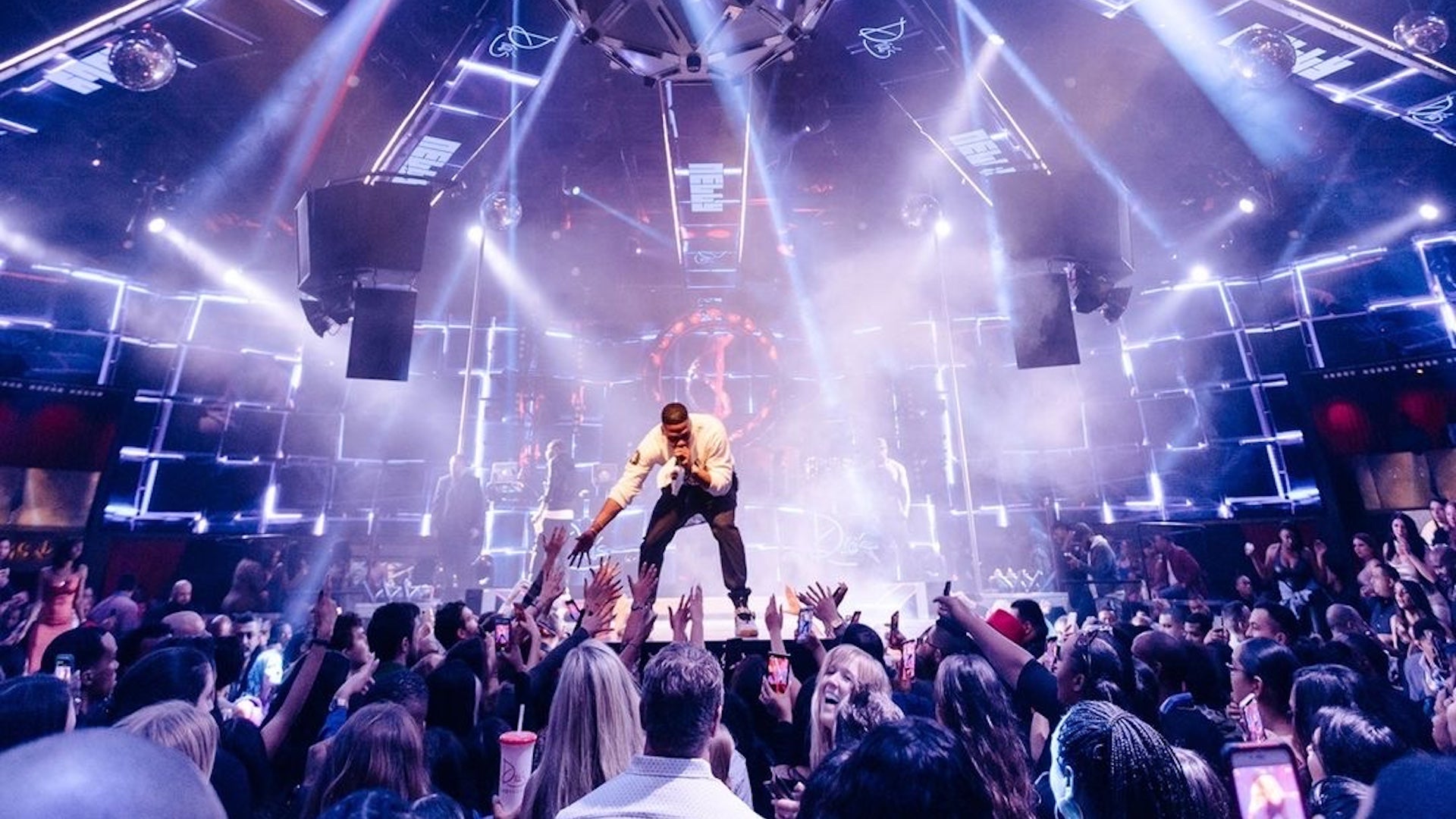 Person standing on a stage performing for a crowd under bright lights