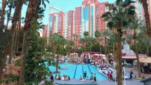 Pool surrounded by flamingo statues and pool deck furniture with a hotel in the background