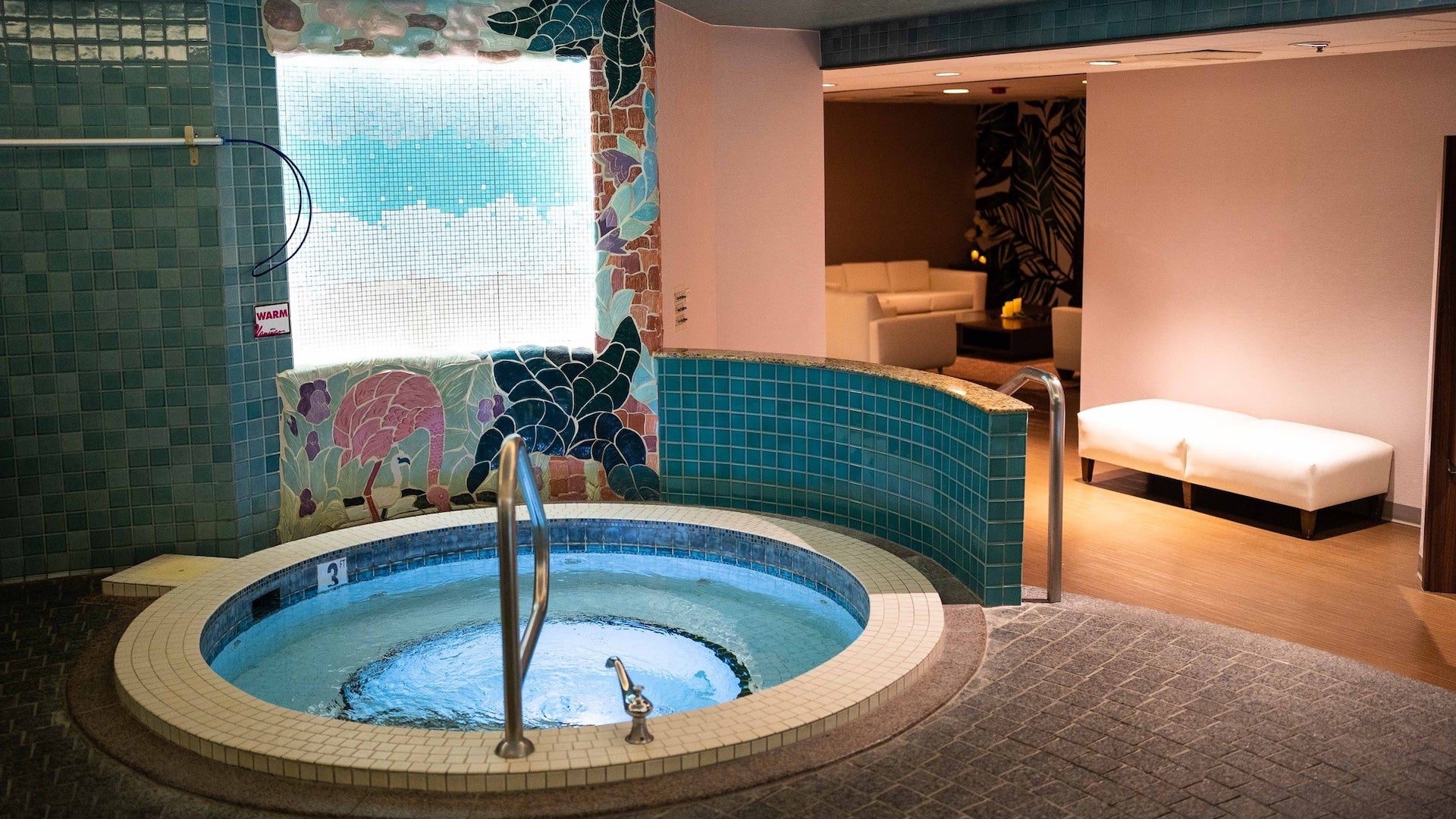 Interior shot of a small round hot tub with blue tile walls and a daybed in the background